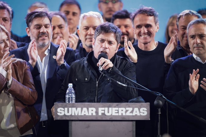 Axel Kicillof da un discurso tras el triunfo electoral, rodeado de su equipo en el escenario con el cartel "Sumar fuerzas".